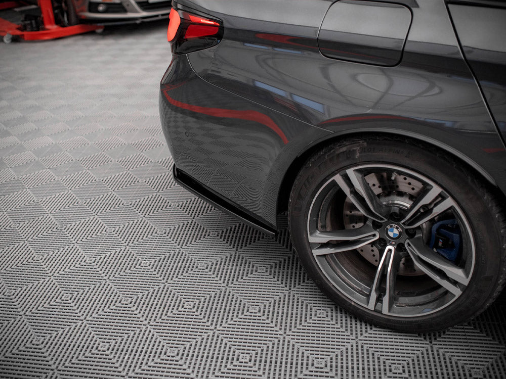 A dark gray car's rear wheel is stationary on a patterned garage floor, with a red vehicle lift partially visible in the background.