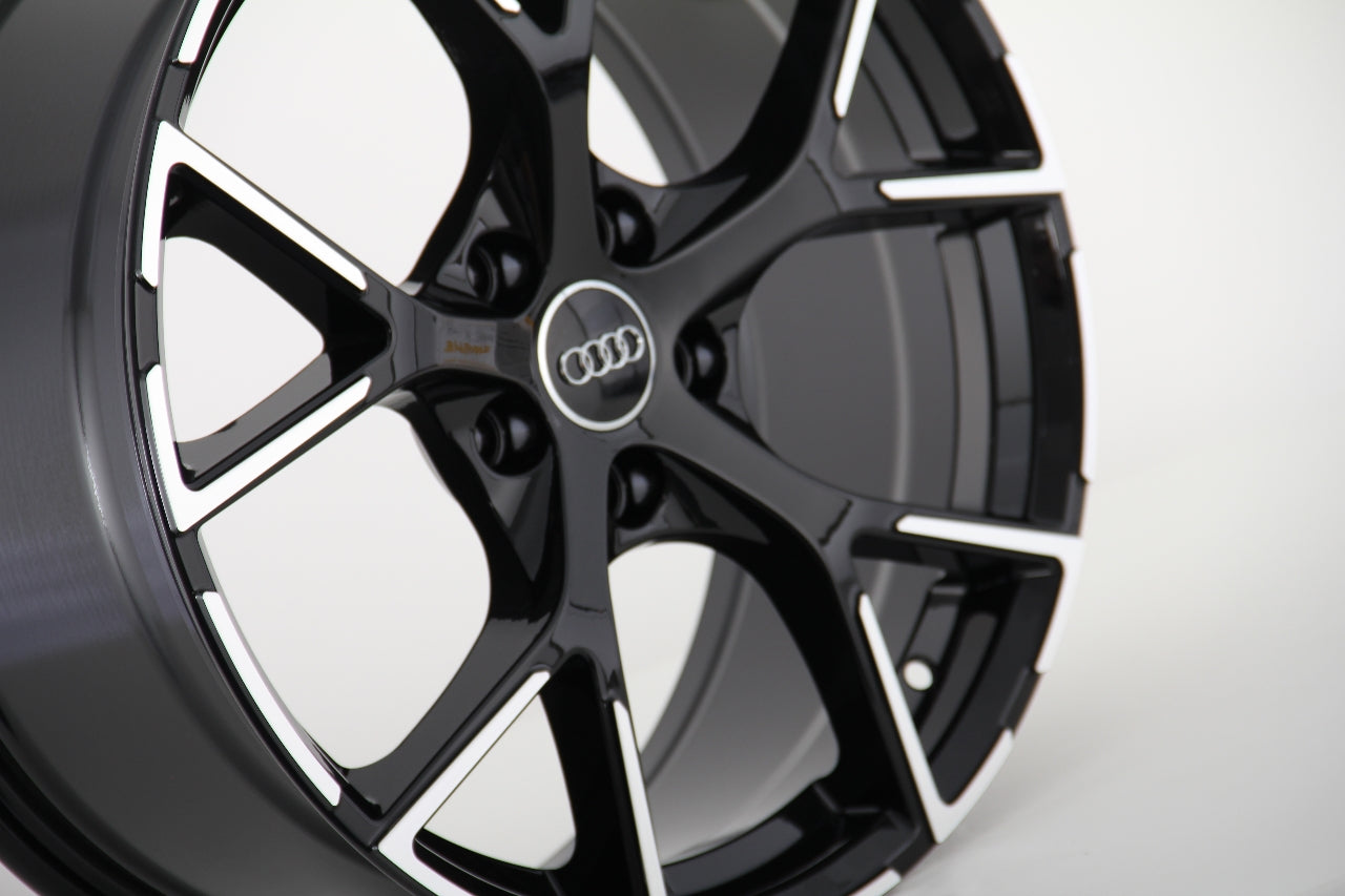 Black and silver alloy wheel, featuring a five-spoke design with the Audi logo at the center, set against a plain white background.