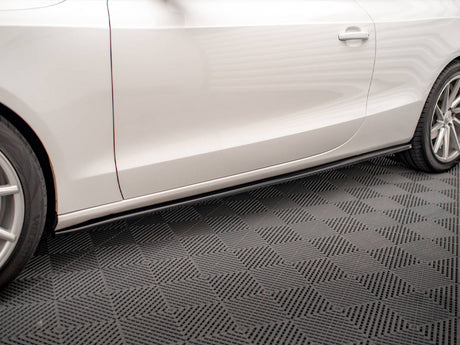 A white car with sleek design features rests on a textured garage floor, showcasing its side profile with visible wheel rims and a door handle.