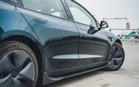 A blue car is parked on a concrete road, showcasing its sleek design and black rims. In the background, there's industrial equipment and a traffic sign. The tire reads "MICHELIN 235/45 ZR 18".