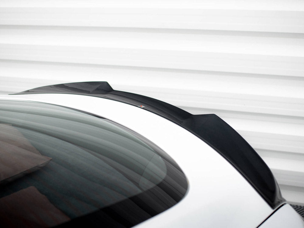 A sleek black car spoiler is mounted on a white vehicle's rear, with a reflective glass surface, set against a striped, white metal background.