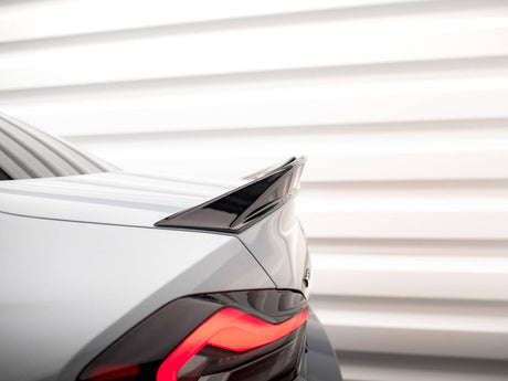 A sleek car's rear, featuring a glossy black spoiler, displays bright red taillights. It is set against a background of evenly spaced horizontal white panels.