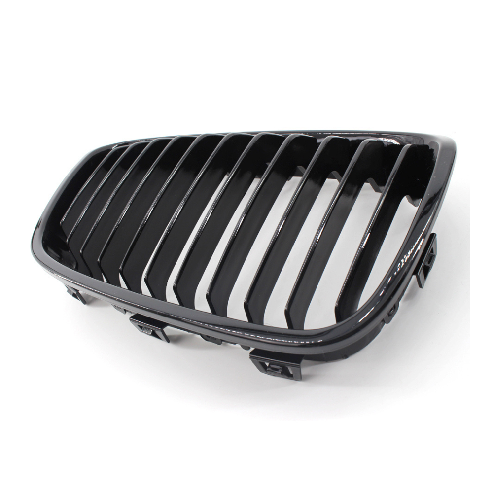 A black car grille with vertical slats rests on a white surface, showcasing its glossy finish and sleek design.