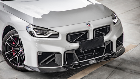 A sleek, white sports car stands in a garage. The car features a prominent grille, detailed headlights, and a carbon fiber front bumper. The tire reads "Pirelli".