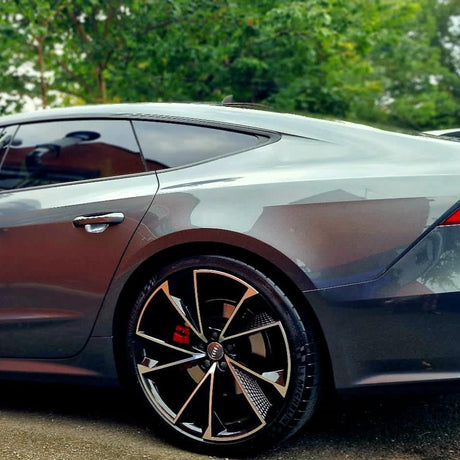 A sleek silver car is parked, showcasing its modern wheel design and smooth body curves. Trees and greenery create a natural backdrop.