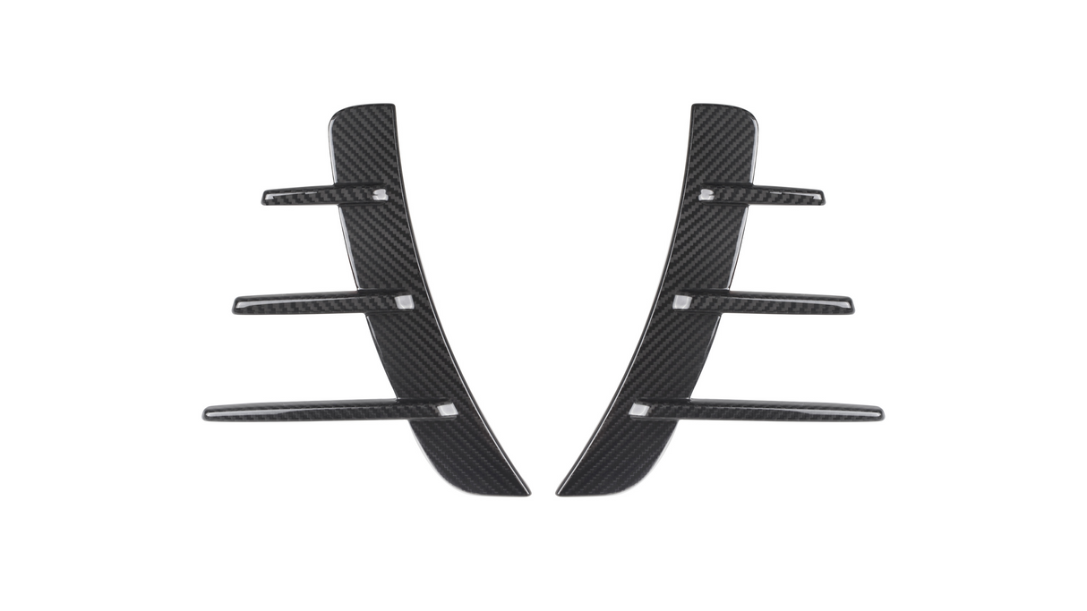 Two black carbon fiber pieces with three horizontal fins each are symmetrically aligned. They are set against a plain white background, suggesting automotive parts.