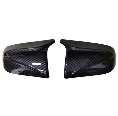 Two glossy carbon fiber car mirror covers, resting side by side against a white background, highlighting their sleek, aerodynamic design and polished finish.