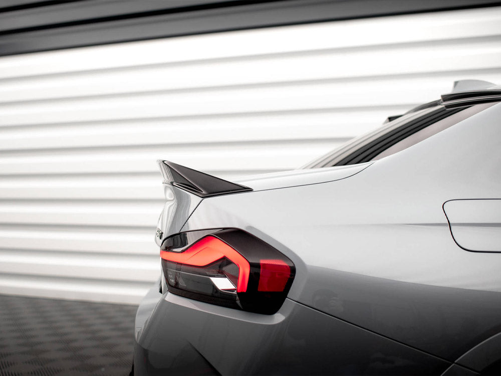 A sleek car's rear with an illuminated taillight and prominent spoiler, parked in front of a white, horizontal-panel garage door.
