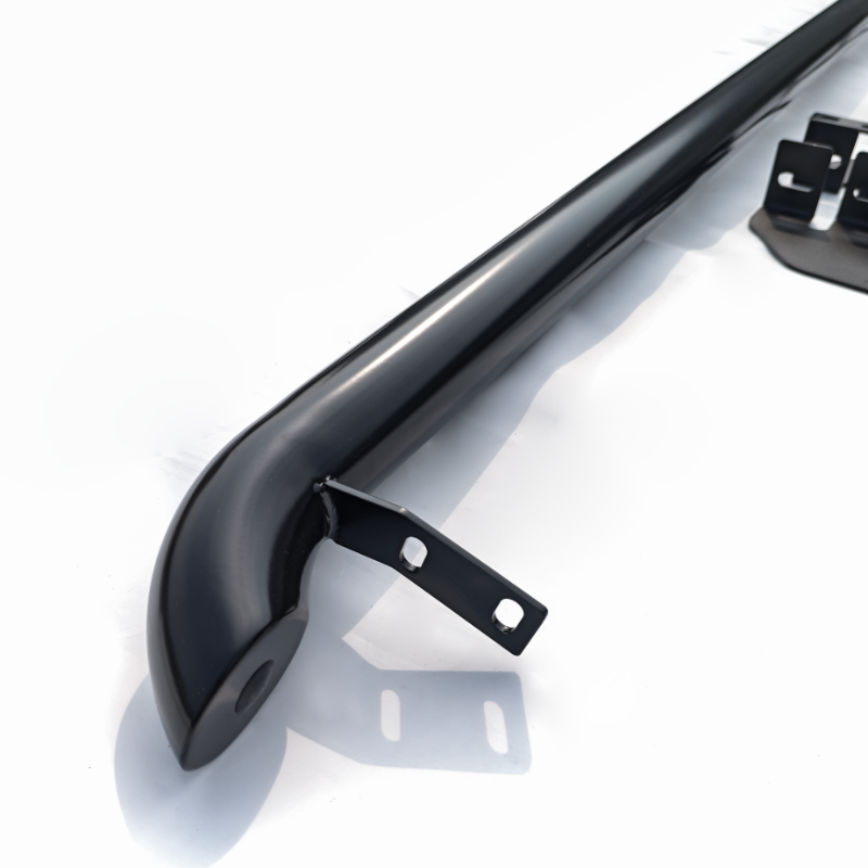 A black metal bar with mounting brackets is positioned on a plain white surface, likely part of a vehicle accessory or structural component.