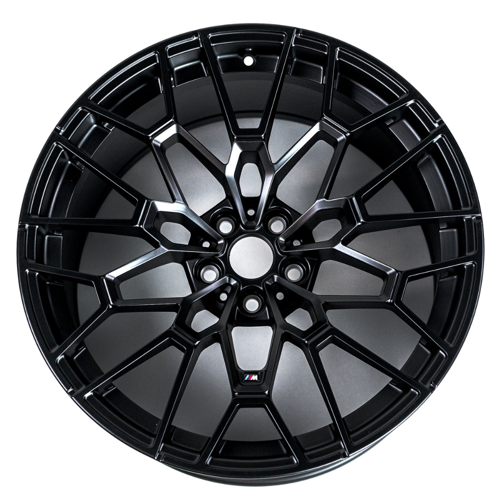 A black alloy wheel features a complex, multi-spoke design. It's displayed against a plain, white background. There is a small logo with the letter "M" in color.