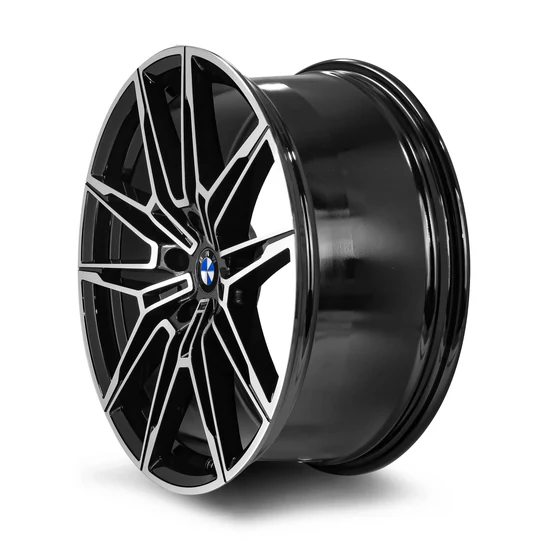 A black, multi-spoke alloy wheel with a central emblem sits in a plain, white background, highlighting its polished finish and intricate design.