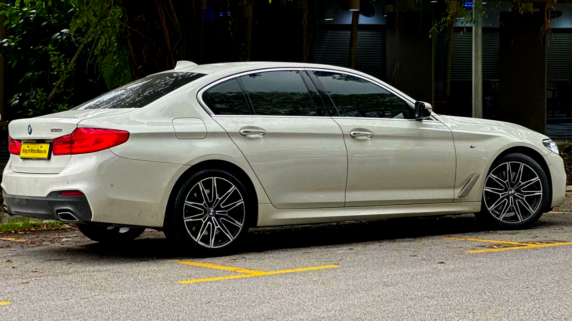 A white BMW 530i sedan is parked on a street, surrounded by greenery. The license plate reads "King of Rims Malaysia."