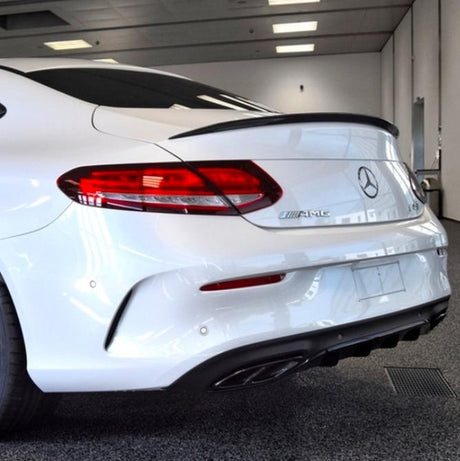 A white Mercedes-Benz AMG car is stationary in a well-lit indoor showroom. The emphasis is on its rear, featuring sleek taillights, a glossy finish, and dual exhausts.