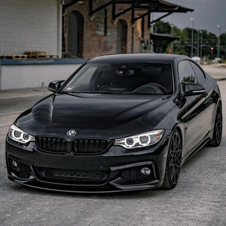 A sleek black BMW car is parked in front of a weathered brick building with an industrial setting, featuring distinct curved headlights and alloy wheels.