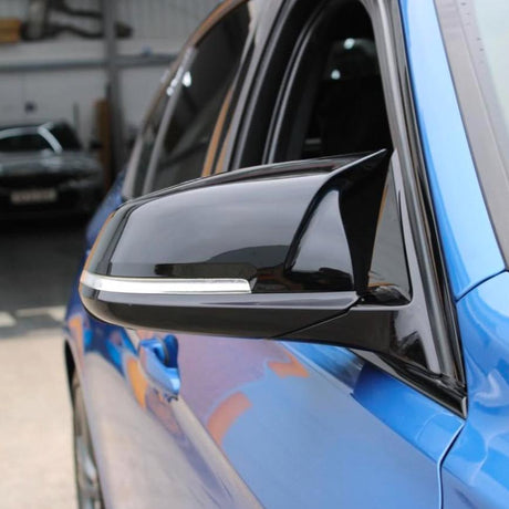 A black side mirror is attached to a blue car, reflecting light. The car is parked in a garage with another vehicle visible in the blurred background.