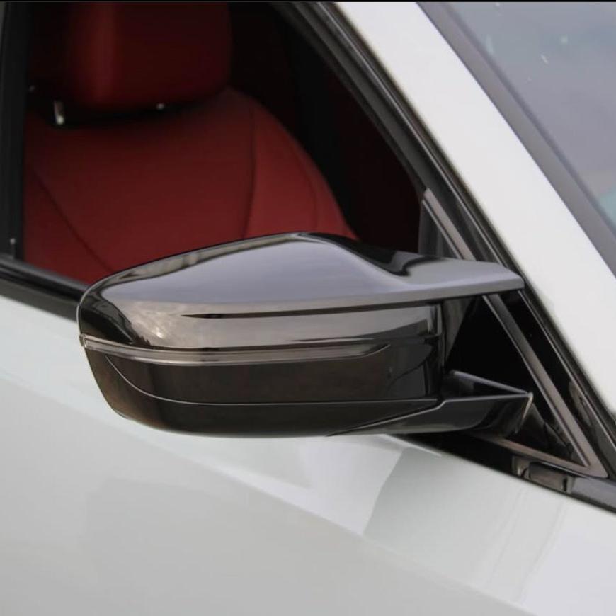 A sleek, black side mirror protrudes from a white car door, reflecting the surroundings. The car interior is visible with a red seat, suggesting a luxurious design.