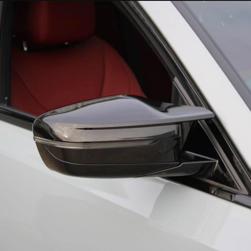 Side mirror with a sleek design attached to a white vehicle, facing outward. The interior features a red seat, visible through the window.