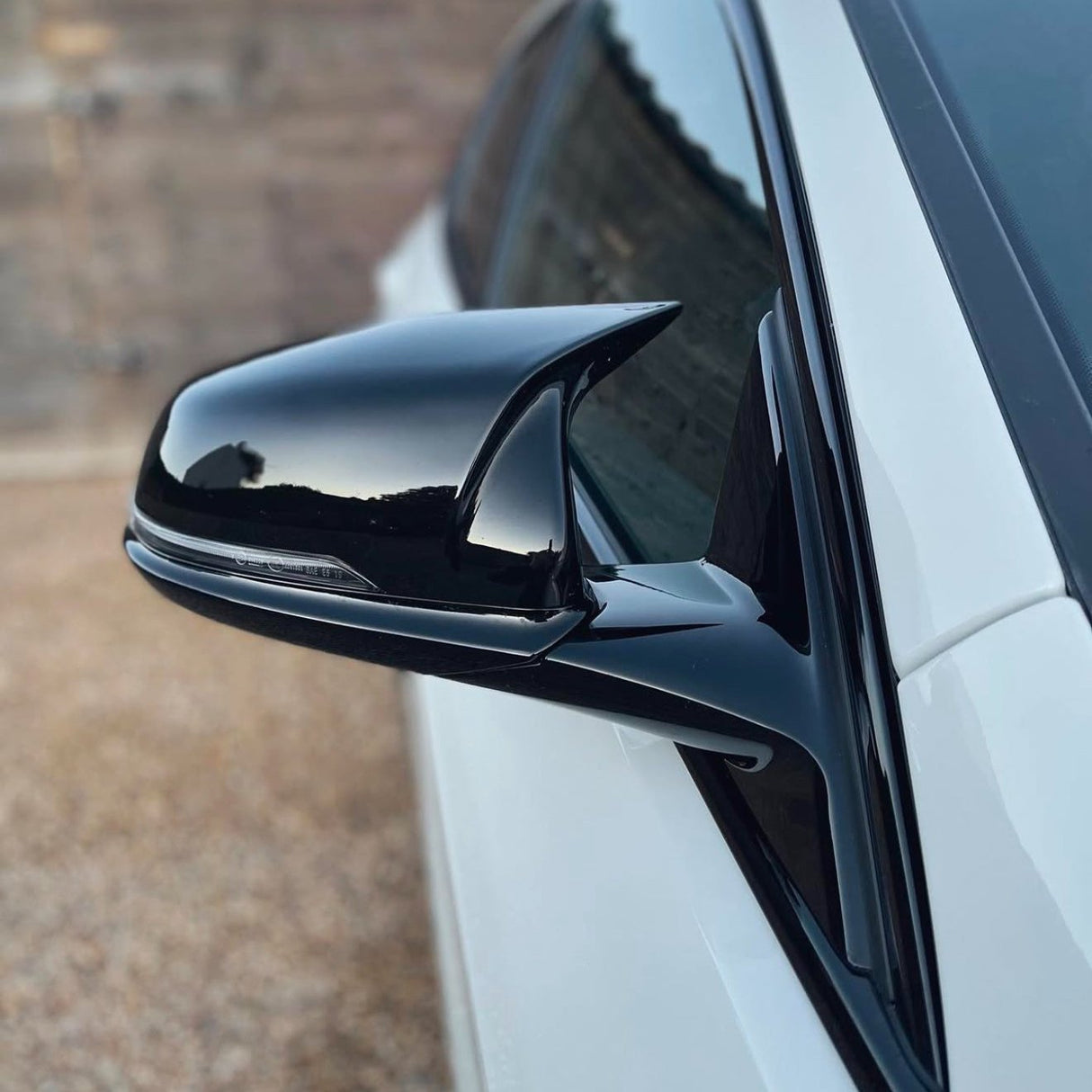 A black side mirror, attached to a white car, reflects the sky. The background features a blurred, earthy-colored surface with a textured pattern.