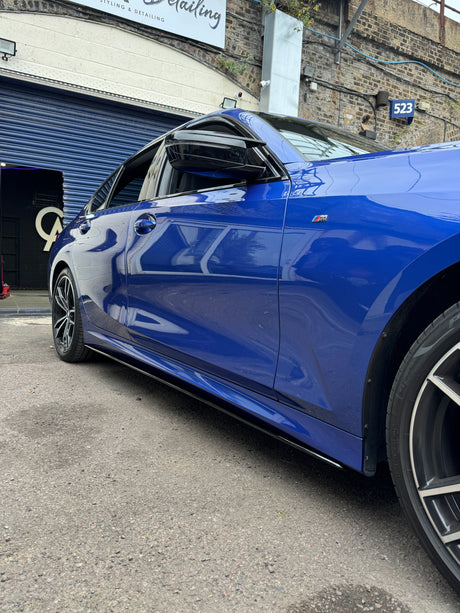 A blue car parked with its window slightly open, located outside a detailing garage beneath a brick archway. The garage has a sign reading “Styling & Detailing” and a number “523.”