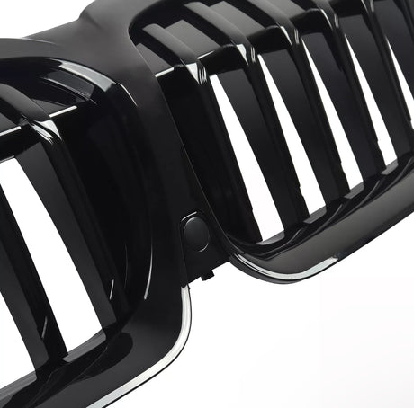 A black, glossy car grille with vertical slats is shown in close-up detail. The grille's shiny surface and precise design indicate a high-quality automotive component.