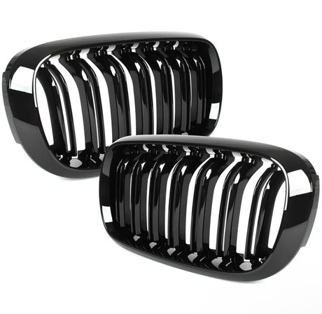 Two glossy black kidney-shaped car grilles with vertical slats are displayed against a white background. They are stacked, with one partially overlapping the other, suggesting automotive components.