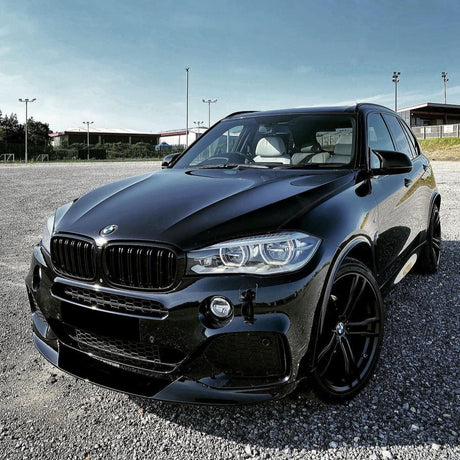 A sleek black BMW SUV is parked on a gravel lot. It sits under a clear blue sky, near empty sports fields with pole lights.