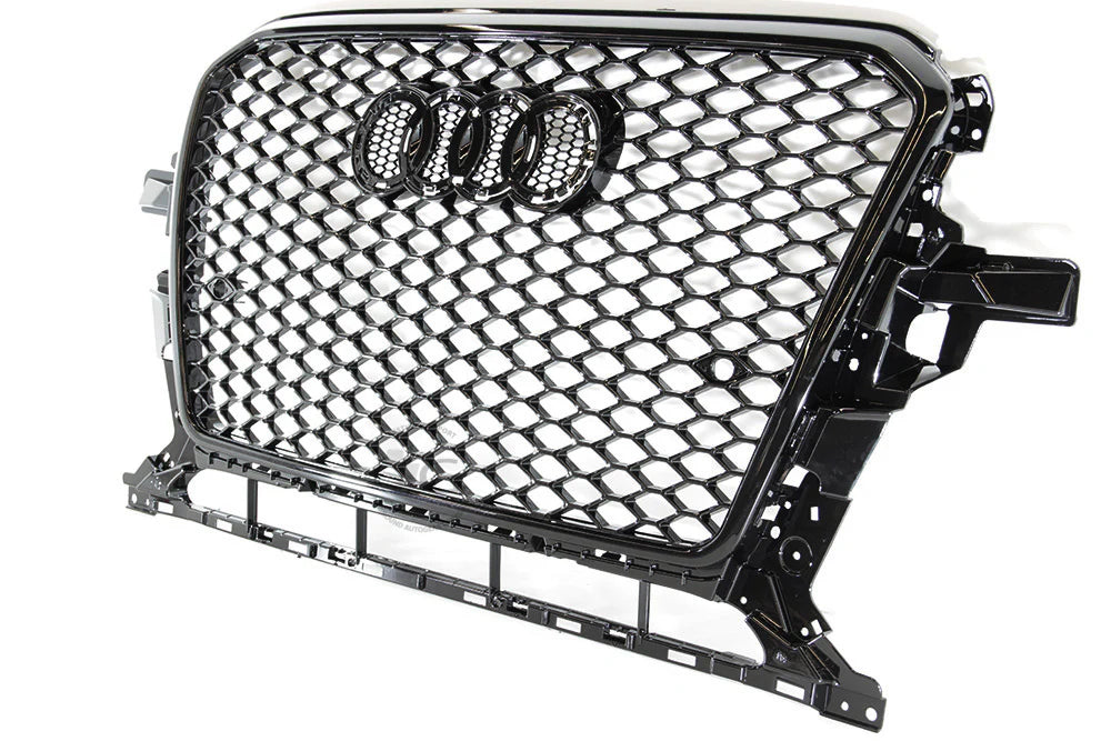 A black car grille with a honeycomb design features four interlinked rings in the center. It is suspended against a plain white background.