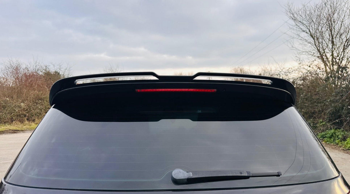 A car with a rear window featuring a wiper and a spoiler, surrounded by overcast skies and leafless trees.
