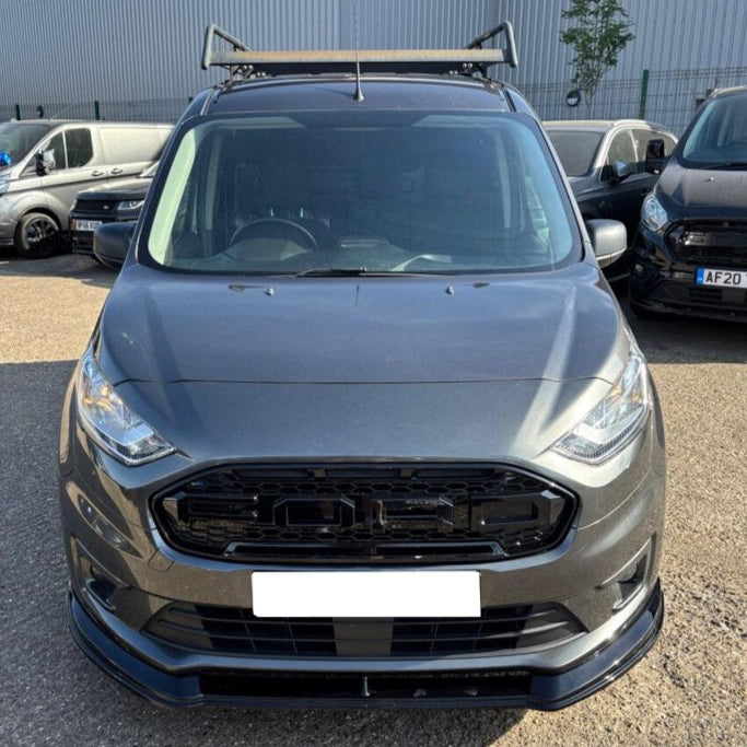 A gray van is parked outdoors, directly facing the viewer. It has a roof rack and is surrounded by other vehicles in an industrial area. License plate reads: "AF20".