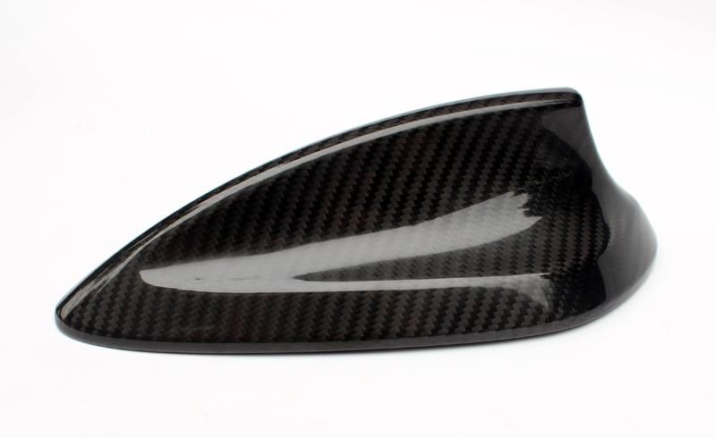 A carbon fiber car antenna cover with a sleek, aerodynamic design rests on a plain, white background.