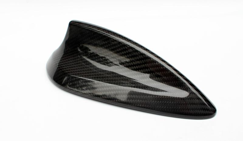 A carbon fiber car antenna is resting on a plain white surface, showcasing a sleek, aerodynamic design with a glossy finish and a subtle checkered pattern.