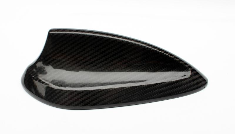 A carbon fiber car side mirror cover resting on a white background, showcasing a glossy finish and textured pattern, highlighting its sleek design and lightweight material.