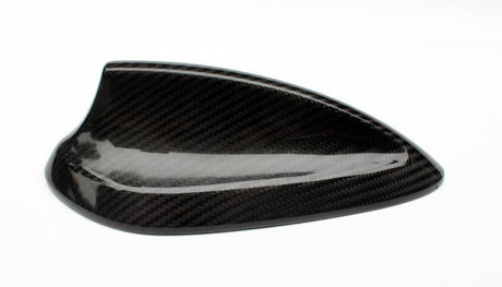 A carbon fiber car side mirror cover resting on a white background, showcasing a glossy finish and textured pattern, highlighting its sleek design and lightweight material.