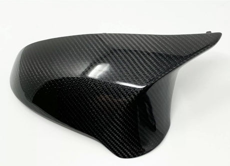 A smooth, black carbon fiber car mirror cover with a glossy finish is resting on a plain white surface, highlighting its sleek design and reflective texture.