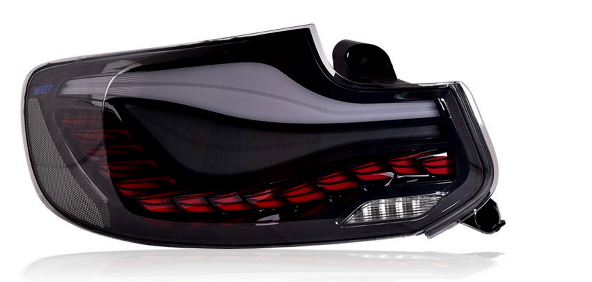 A sleek, dark automotive tail light with a dynamic red pattern and LED indicator, set on a reflective white surface. The label reads “OLED.”
