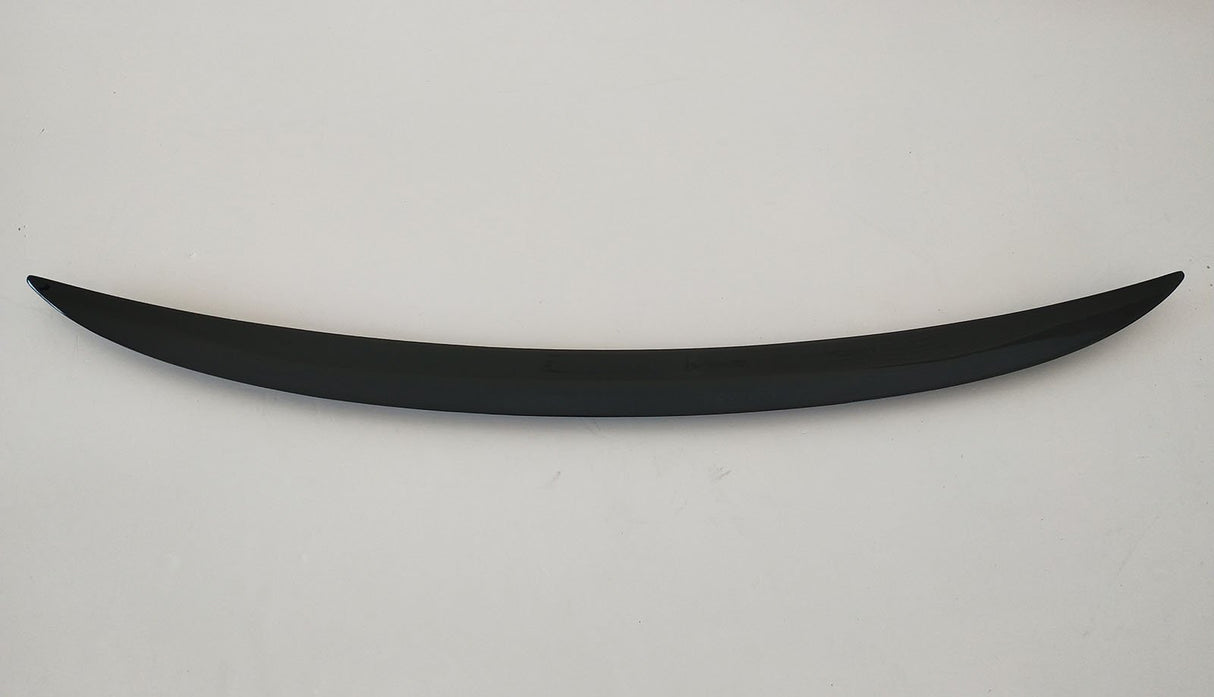 A curved, sleek, black object rests horizontally on a plain, light-colored background, resembling a minimalist sculpture or car spoiler.