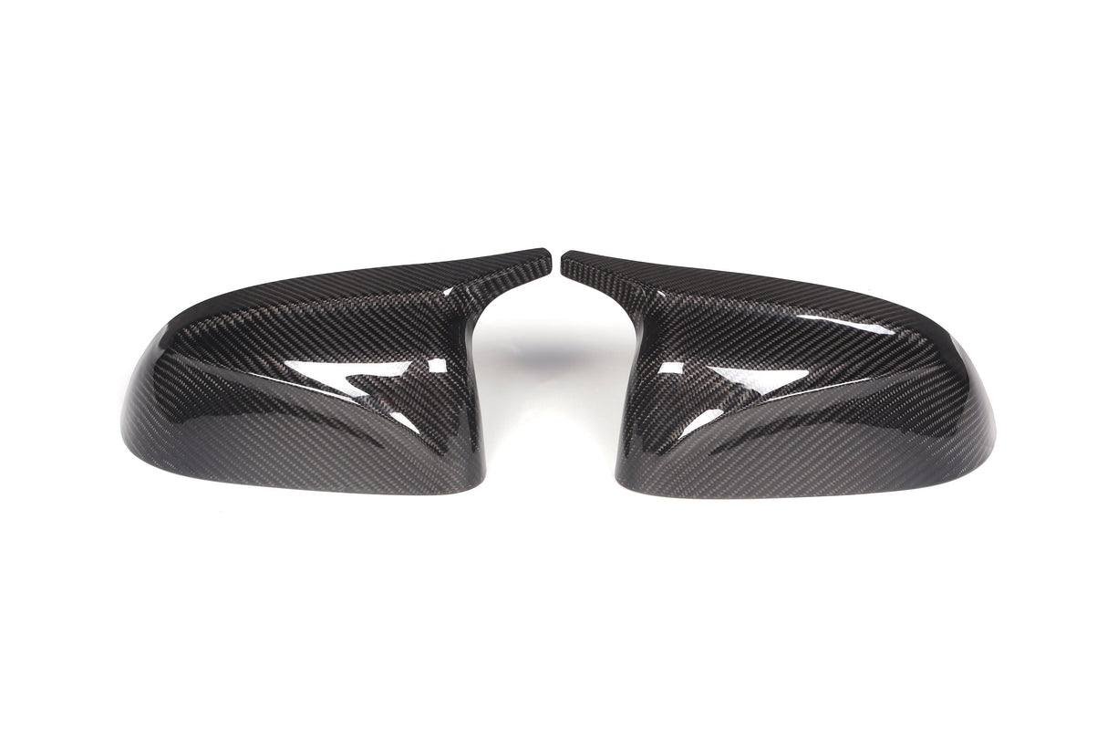Two carbon fiber side mirror covers face each other, showing a glossy finish and distinct weave pattern, placed on a white background.
