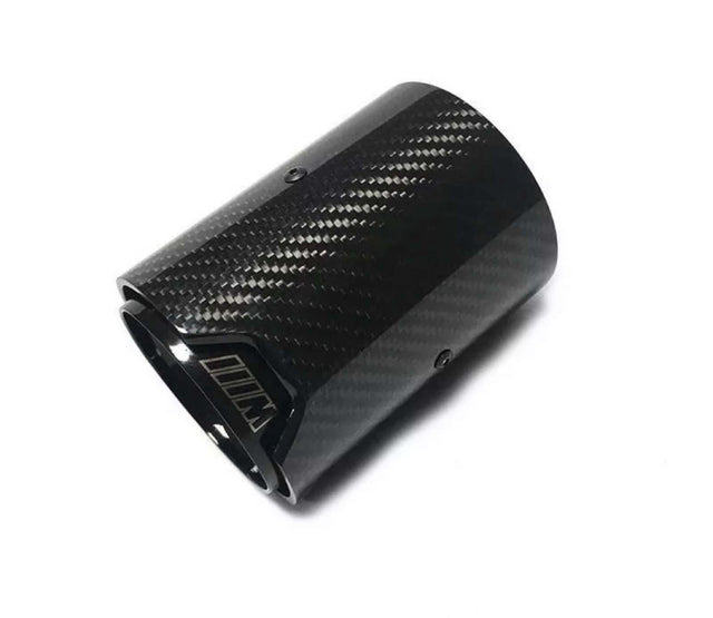 A carbon fiber exhaust tip lies against a plain white background. The surface has a textured pattern. The inner edge features a logo or marking resembling "///M."