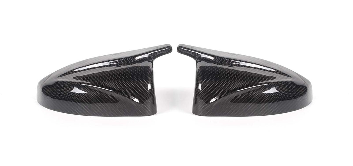Two carbon fiber side mirror covers rest on a white surface, showcasing a glossy finish and intricate weave pattern, appearing symmetrically aligned.