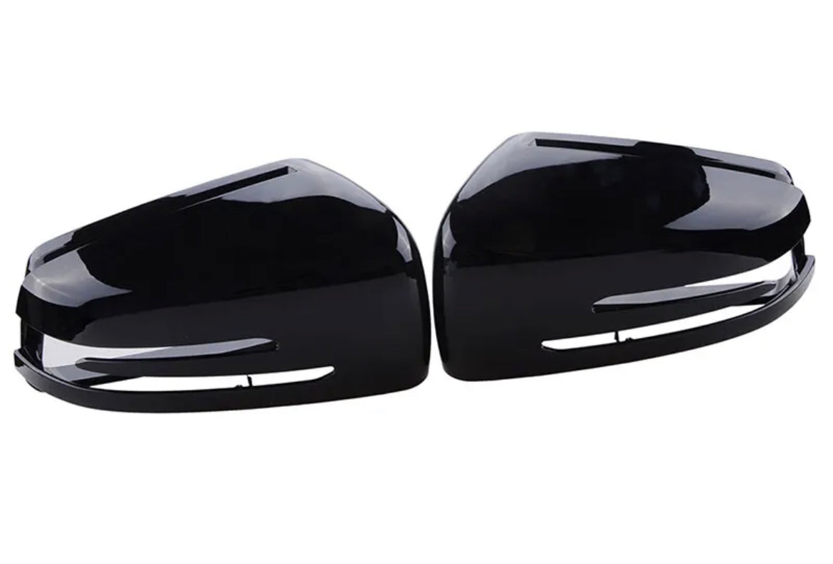 Two glossy black side mirror covers are positioned symmetrically, facing each other, against a plain white background.