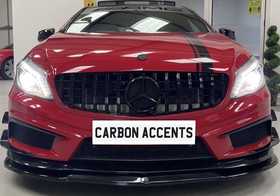 A red sports car with illuminated headlights is parked indoors, featuring black grille and stripes. A sign in front reads "CARBON ACCENTS." Decorative plants and another car are visible in the background.