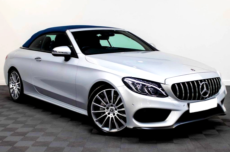 Silver convertible car, parked in an indoor showroom. The vehicle features a blue soft-top roof, sleek body lines, and distinctive front grille with a logo. The floor is checkered tile.