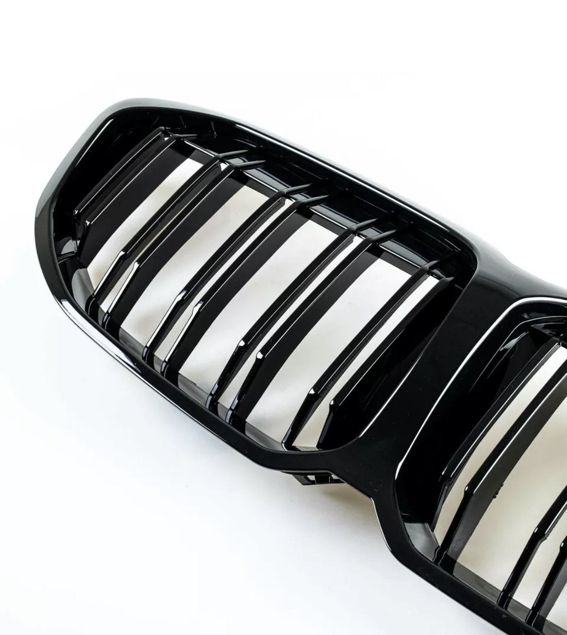 Black car grille with vertical bars, reflecting light. It rests on a plain white background, highlighting the glossy finish and sleek design.