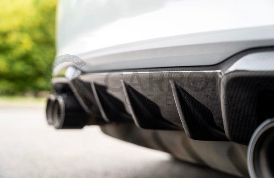 Car rear diffuser with exhaust pipes, surrounded by blurred greenery and pavement. Text reads: "CARBON ACCENTS," faintly visible over the image in gray.