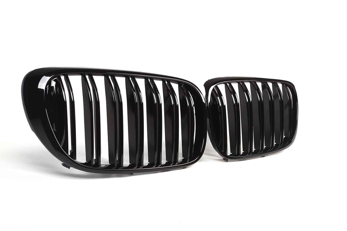 Two glossy black car grilles, featuring vertical slats, are positioned on a plain white background, angled slightly toward each other.