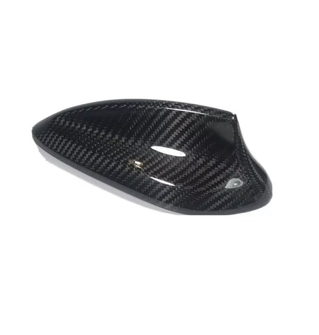 Carbon fiber car side mirror cover, sleek and glossy, resting on a plain white background. The cover exhibits a distinct woven pattern and aerodynamic design, emphasizing high-performance aesthetics.