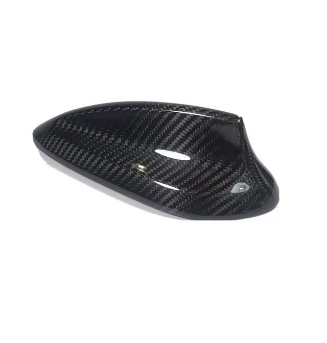 Carbon fiber car side mirror cover, sleek and glossy, resting on a plain white background. The cover exhibits a distinct woven pattern and aerodynamic design, emphasizing high-performance aesthetics.