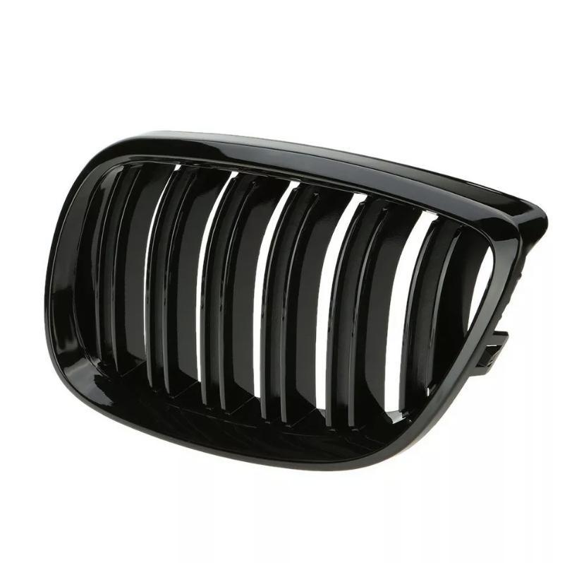 A shiny, black automotive grille with vertical slats is lying on a plain, white background, likely for use as a vehicle front intake or trim component.