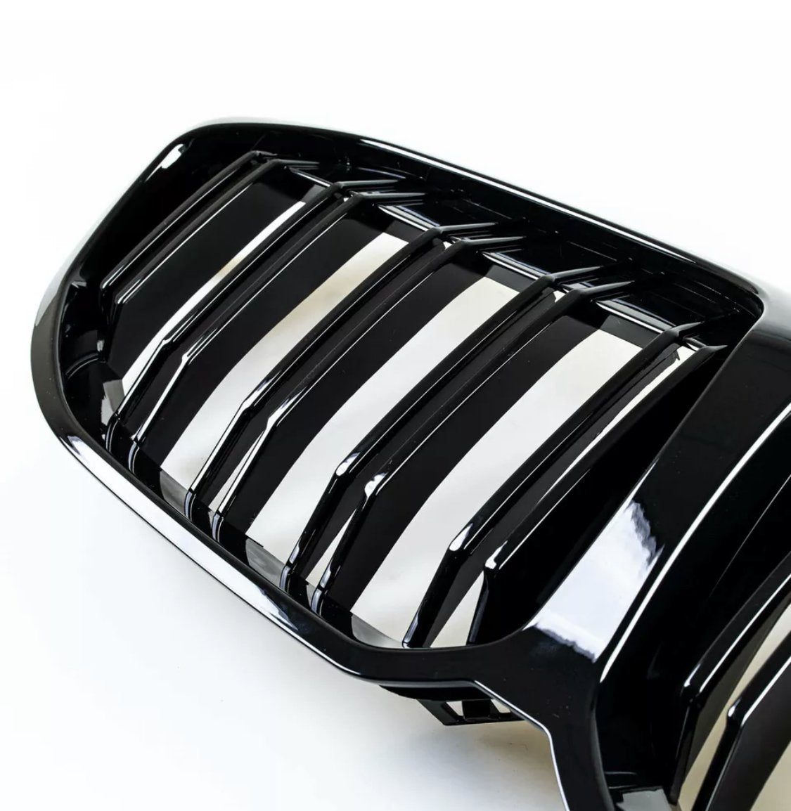 A glossy black car grille with vertical slats sits on a white background, showcasing its reflective surface and designed for air intake efficiency in a vehicle's front exterior.
