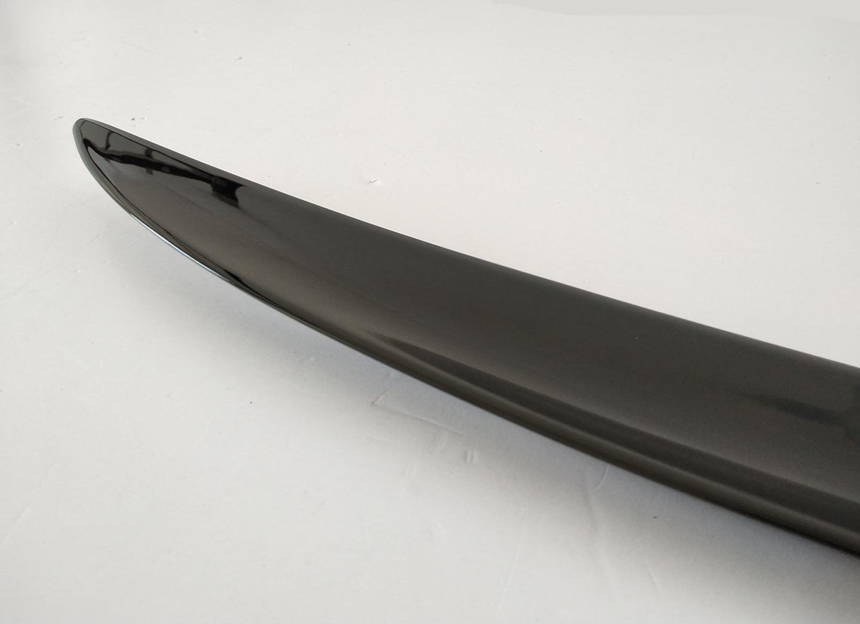 Shiny black car spoiler, curving slightly upward, sits on a smooth, light gray surface.